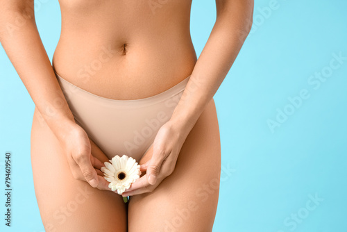 Beautiful young woman in panties with gerbera flower on blue background, closeup © Pixel-Shot