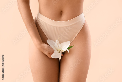 Beautiful young woman in panties with lily flower on beige background, closeup