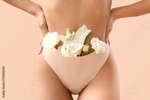 Beautiful young woman in panties with flowers on beige background, closeup