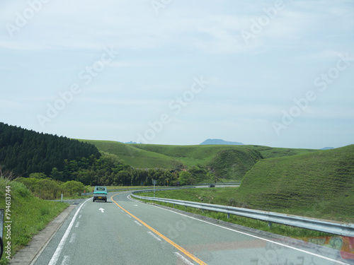 Travelling on Kyushu, driving to distant Mount Aso famous volcano caldera contour on lonely road with lush green grass valley on roadsides on sunny day