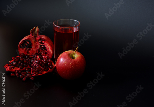 A glass of juice from a mixture of pomegranate and red apple on a black background, next to ripe fruits.
