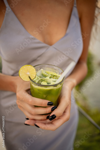 Green vegetable smoothie with lemon and ice in woman hands. Healthy diet concepgt