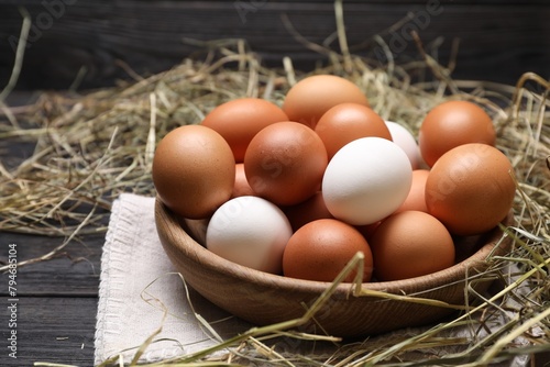 Fresh chicken eggs in bowl and dried hay on black wooden table