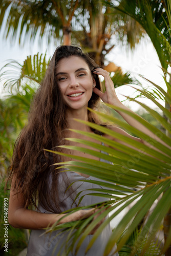 Portrait of young and beautiful woman with perfect smooth skin in tropical leaves smiling and touch the hair. Concept of natural cosmetics and skincare