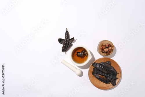 High angle view photo, with some locust fruits placed on wooden dish, a wooden podium with anise above and a mortar with brown liquid next to a pestle. Copy space for text © Tuan  Nguyen 