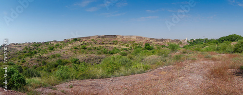 Panoramic view of wall of Mehrangarh fort from Rao Jodha desert rock park, Jodhpur, India. Green vegetation in the foreground with rocky landscape of the desert park.