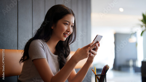 Asian teenage student woman using smartphone to chatting with friends and surfing social media after studying and reading information in paperwork to learning about education knowledge in cafe