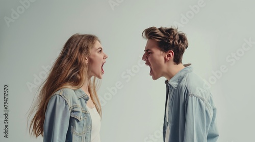 Side view of an angry young couple shouting at each other on a gray background . photo