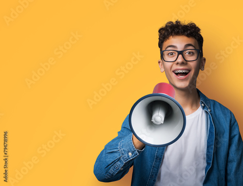 Funny happy brunette young man wear glasses dent dental tooth braces brackets advertise use mega phone megaphone loudspeaker open mouth, isolated over yellow background. Sales ad concept
