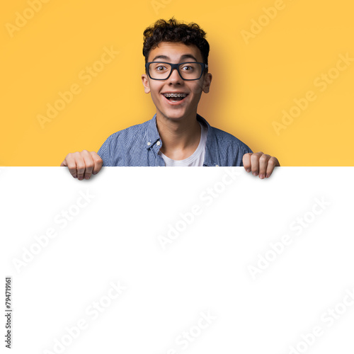 Very happy man wear eye glasses, braces stand behind, peep blank empty banner mockup sign board signboard, advertise show area for sale slogan text isolated yellow background. Dental care ad