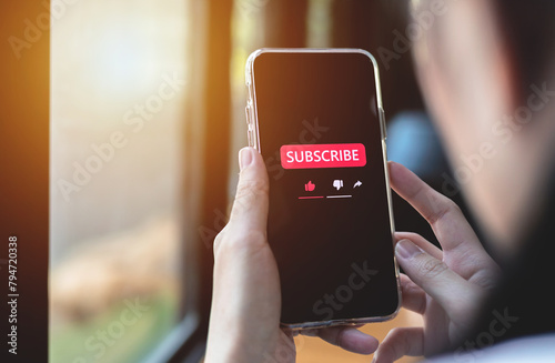Close-up view of a woman using a smartphone to press red subscribe button on online media. Concepts of technology and following news, hot trends and new content on social media