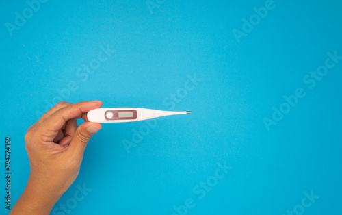 Close-up of a hand holding a medical thermometer with indicators of high body temperature on a blue background.