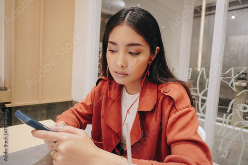 Close up portrait of young Asian woman using smartphone with serious expression inside a cafe. (ID: 794733178)