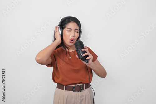 Overjoyed young woman wearing brown shirt and headphone to listen music and singing along isolated over white background. (ID: 794739158)