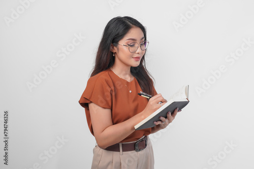 Young Asian women holding book and pen writing task and note in the notebook standing over white background.