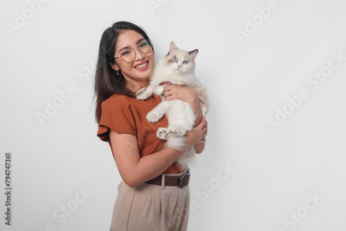 Portrait of young Asian woman in brown shirt holding her ragdoll cat and smiling to the camera isolated over white background.