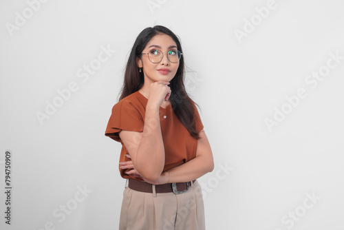 Pensive and thoughtful young casual girl wearing a brown shirt and eyeglasses looking aside isolated over white background. © Reezky