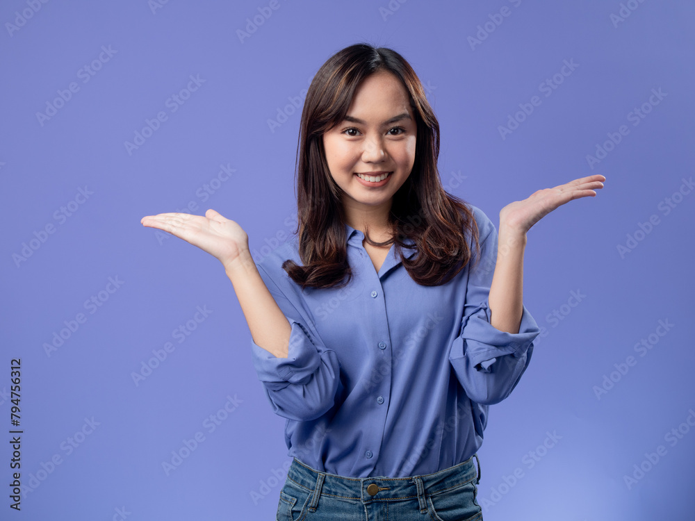 A young Asian woman wearing a purple shirt and jeans stands against a solid lavender background, smiling widely with her arms outstretched, expressing joy and welcoming. A young Asian woman wearing a purple shirt and jeans stands against a solid lavender background, smiling widely with her arms outstretched, expressing joy and welcoming.