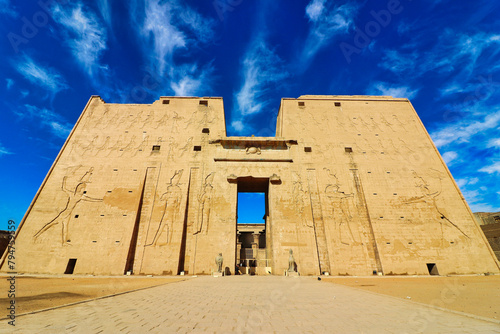 Magnificent view of the Outer Pylons of the Temple of Horus in Edfu built during the Ptolemaic era between 237 to 57 BC with granite statues of Horus against bright blue skies near Aswan,Egypt photo