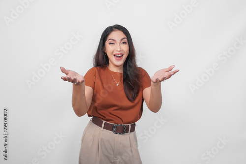 Excited and surprised young Asian woman wearing brown shirt standing isolated over white background. (ID: 794760122)