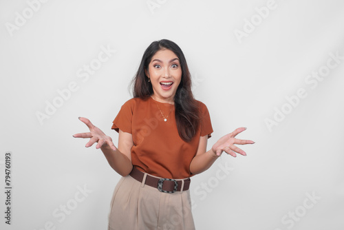 Excited and surprised young Asian woman wearing brown shirt standing isolated over white background. (ID: 794760193)