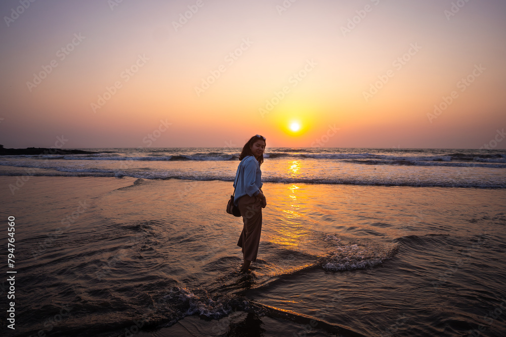 Happy carefree Indian woman  enjoying beautiful sunset on the Goa beach in India
