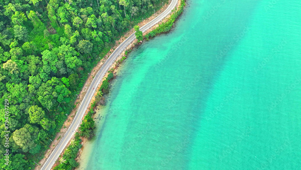 A mesmerizing tropical coastal road, weaving through vibrant greenery, kissed by crystal-clear sea waters. Travel and nature concept. Ko Chang, Trat Province, Thailand. 
