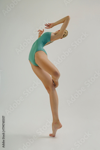 young ballerina in a bodysuit shows ballet steps in motion standing on one leg and spreading her arms