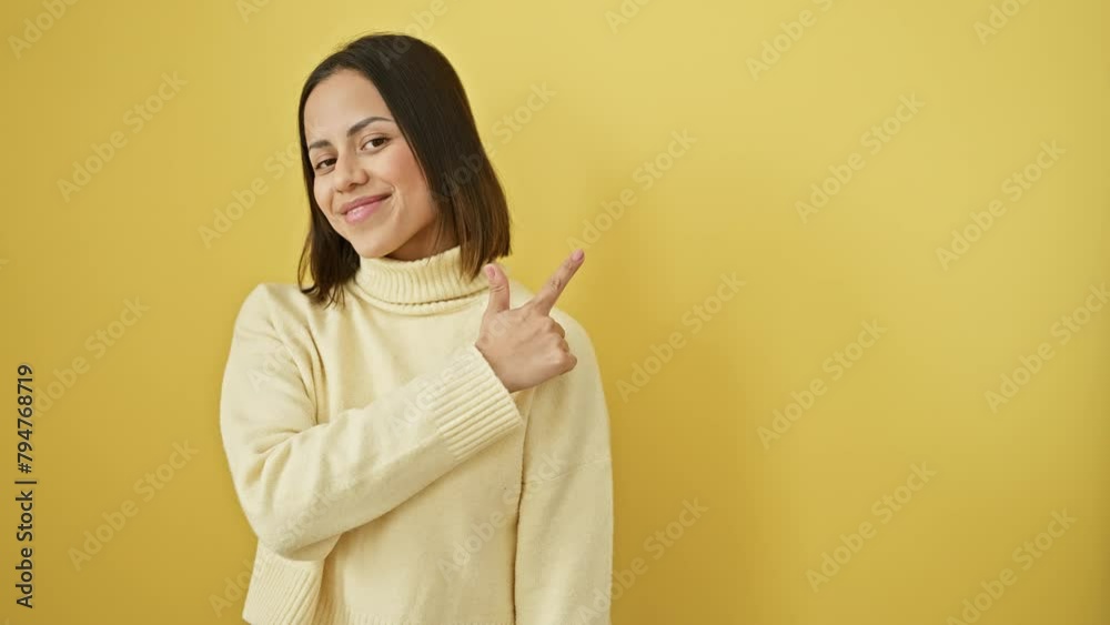 Radiant young hispanic woman in sweater strikes joyful side pose, finger-pointing upwards, showcasing cheerful expression and natural smile against isolated yellow background. Radiant young hispanic woman in sweater strikes joyful side pose, finger-pointing upwards, showcasing cheerful expression and natural smile against isolated yellow background.