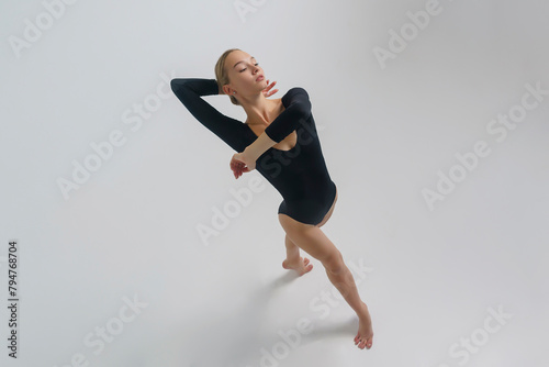 portrait of a young ballerina in a black bodysuit shows ballet steps top view