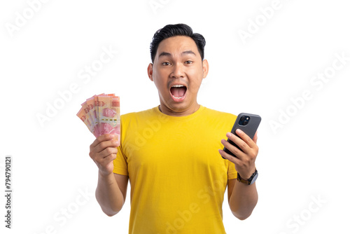 Excited young Asian man holding smartphone and money, looking at camera with surprised expression isolated on white background