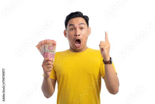 Excited young Asian man holding money and pointing finger up with surprised expression isolated on white background