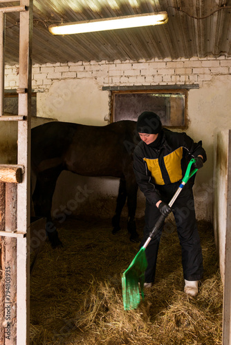 Person mucking out stable with horse