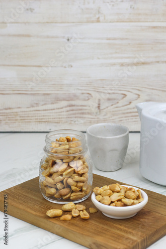 Kacang goreng or fried peanuts in a jar and white plate. Indonesian snack with marble white background, selective focus.