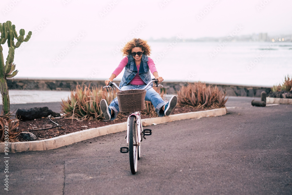 Naklejka premium One young lady riding bike alone on the street with ocean coastline view. Outdoor leisure activity green transport woman. People and healthy lifestyle. Concept of tourist on vacation having fun