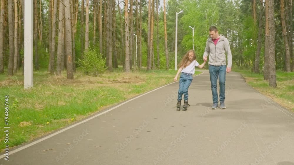 Father and daughter are preparing for roller skating in the fresh air. father's day. The little girl learns to roller skating. Father and daughter are preparing for roller skating in the fresh air. father's day. The little girl learns to roller skating.