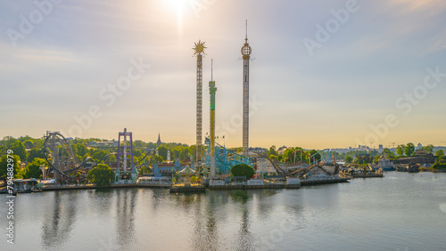 The sun rises on Grona Lund, Stockholms waterfront amusement park, casting a warm glow over the thrill rides and serene waters.