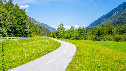 A winding bicycle path cuts through the lush greenery of the Upper Sava Valley with picturesque mountain views under a clear blue sky. Julian Alps, Slovenia