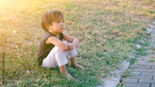Pensive Asian toddler sitting the grassy field.