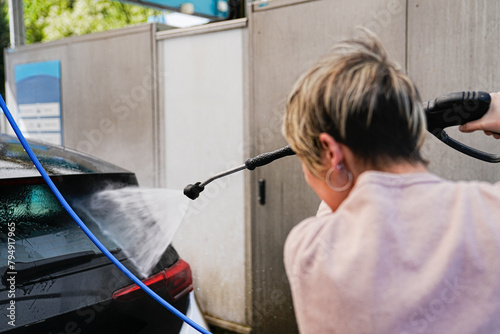 A woman in action, washing her car with a dynamic water jet. photo