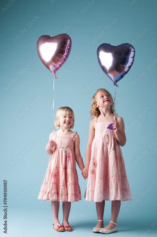 Children, holding hands and sister with heart balloon in studio on blue background for family or party. Birthday, celebration event or happy with smile of girl kids on color backdrop together