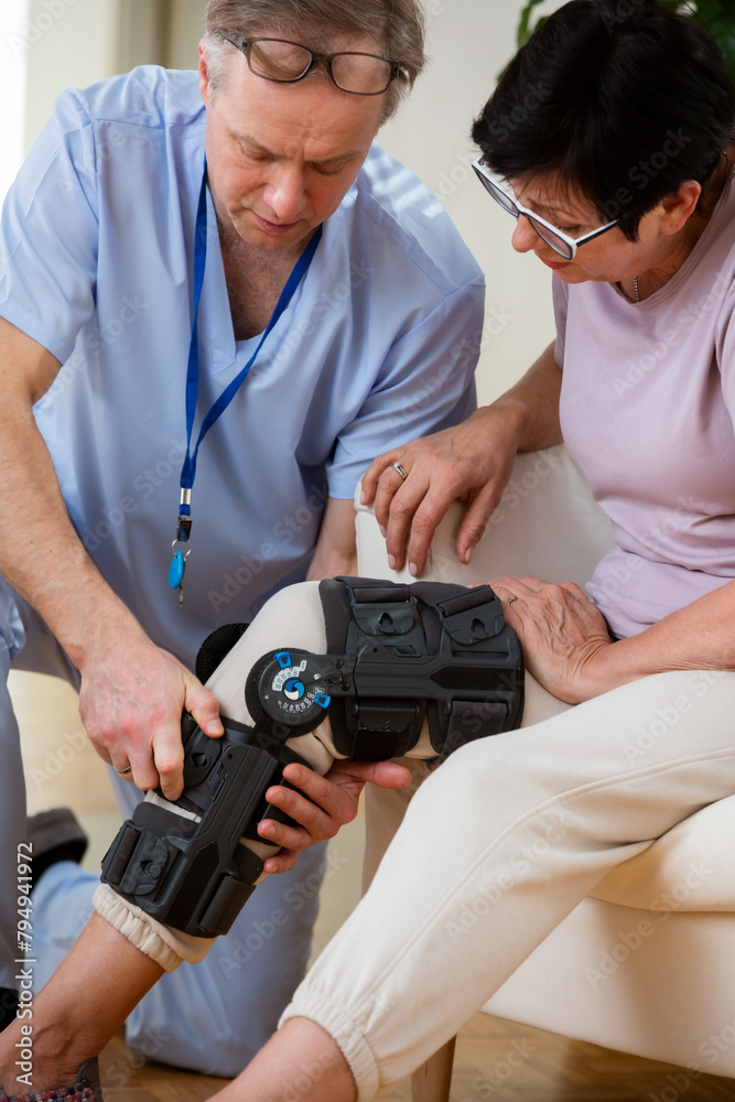 A male nurse helps to put a bondage, medical splint, knee brace on the leg of an elderly female patient who communicates with the attending physician at the clinic or hospital. A male nurse helps to put a bondage, medical splint, knee brace on the leg of an elderly female patient who communicates with the attending physician at the clinic or hospital.