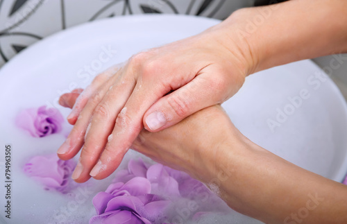 The hands of an adult woman delicately lather each other with floral soap foam in a ceramic bowl sink.