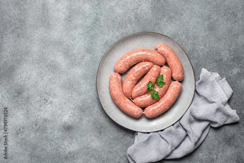 Raw homemade sausages in a plate on a gray concrete background. Top view, flat lay, copy space.