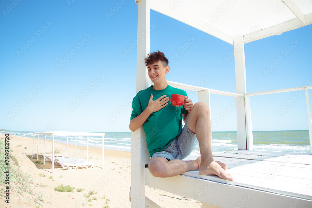 A young attractive man drinks coffee, relaxes and works by the sea.