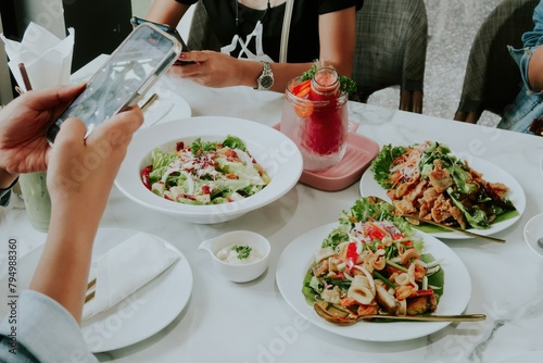 People enjoying a meal together at a restaurant, with one person taking a photo of their food, suitable for social media or dining promotions.
