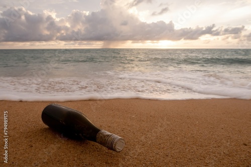 A lone bottle lies on the sand with the ocean in the background, suggesting themes of messages, travel, mystery, and environmental awareness.