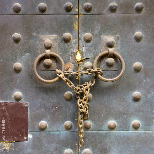 Iron gates with rivets, with two knockers in the form of a ring, tied with a rusty chain