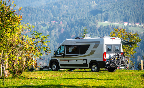 Campervan or motorhome with bicycle rack parked in the nature countryside. Camper van or  motor home is camping in a meadow surrounded by forest and hills. Active family vacation in Slovenia.