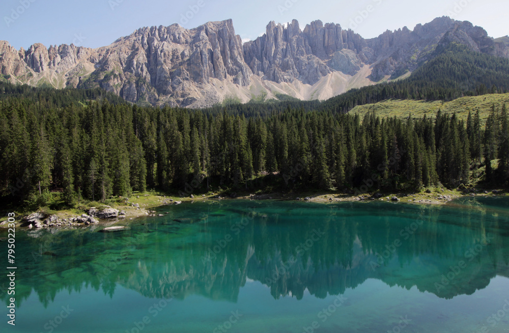 Panoramic photo of the landscape with Lago di Carezza lake and the Latemar mountain massif reflected in the lake and forest in the foreground in the Dolomites, South Tyrol region, Italy